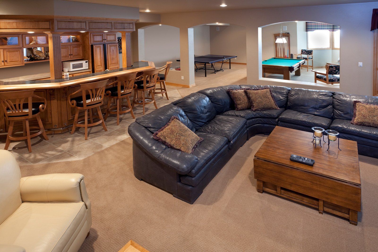 Spacious finished basement with a bar, pool table, and seating areas. Features a large leather sectional sofa and brown wooden accents.