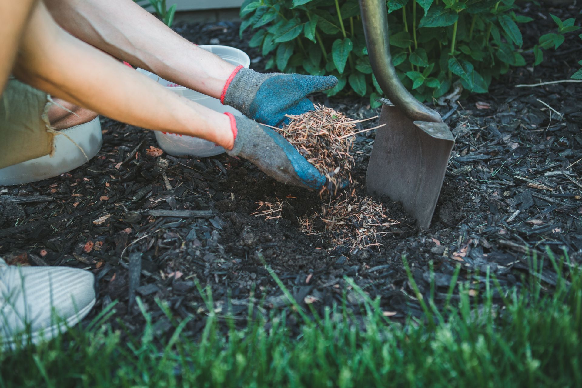 A man is digging mulch in a garden bed, preparing the soil for planting and enhancing plant growth.]