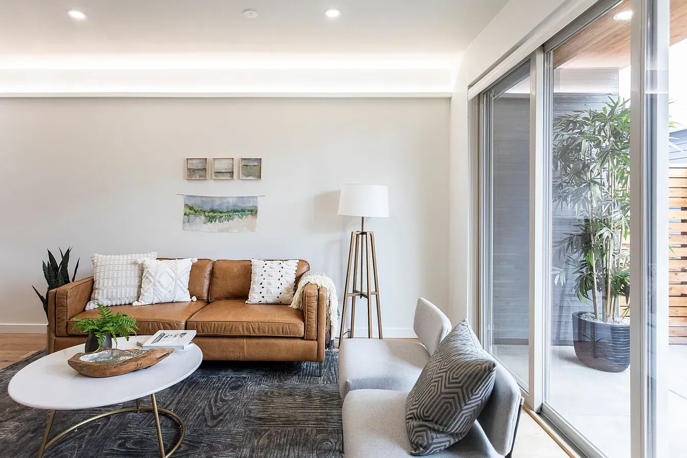 Living room with a brown leather sofa, white walls, and a view to a patio.