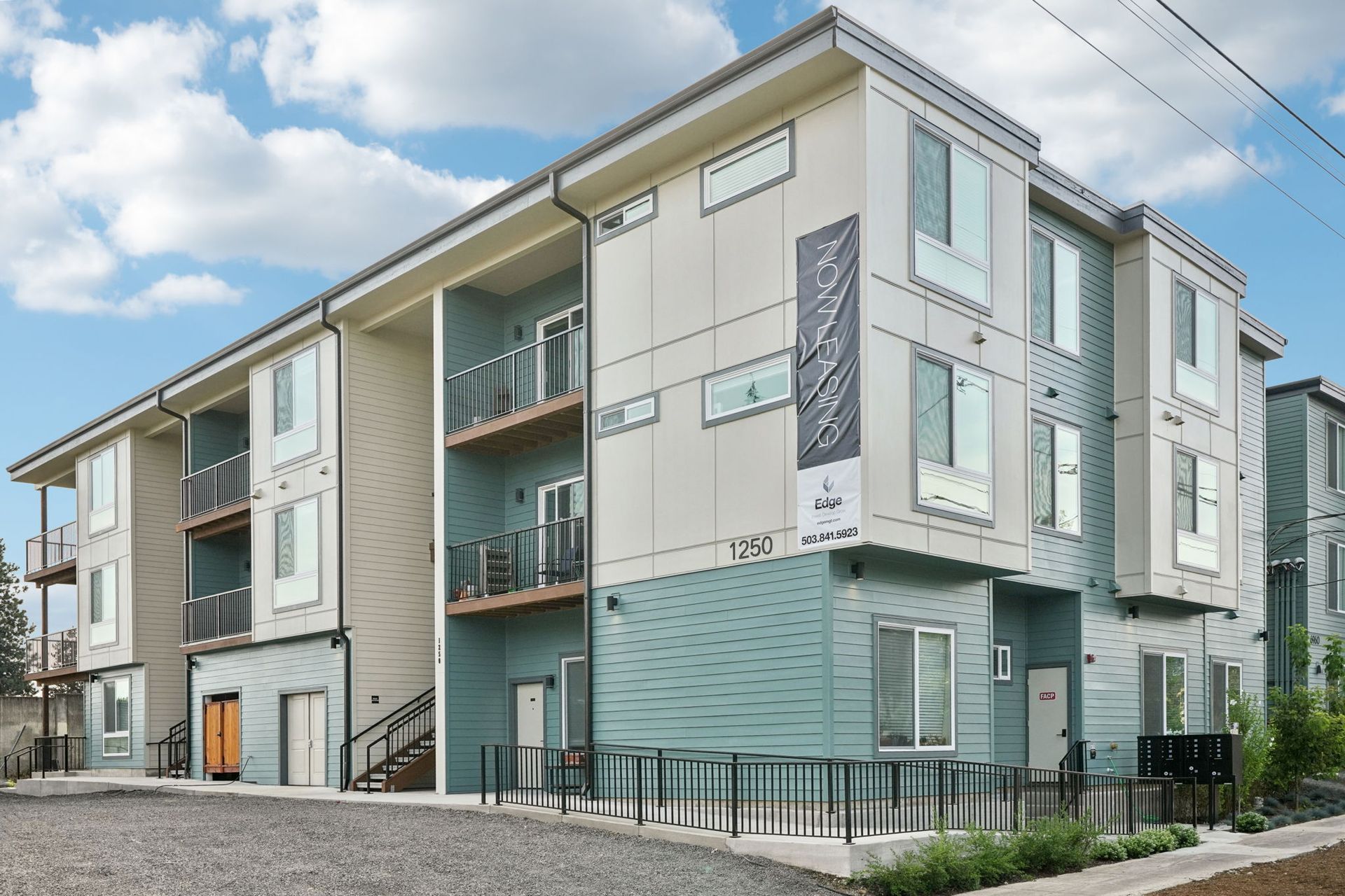 Modern apartment building exterior with blue and gray siding, balconies, and cloudy sky.