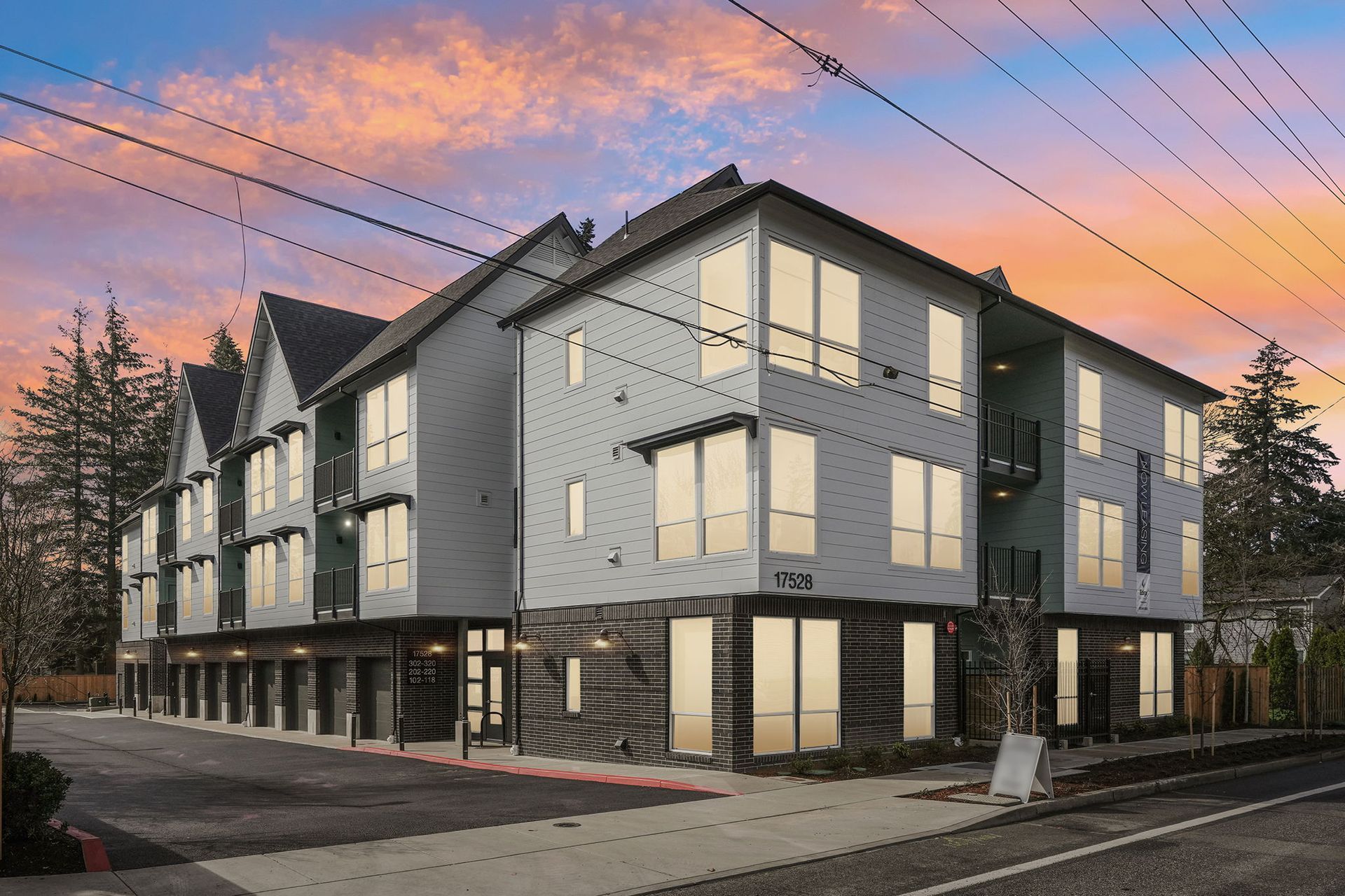 Modern multi-story building with large windows and a gray exterior against a sunset sky.