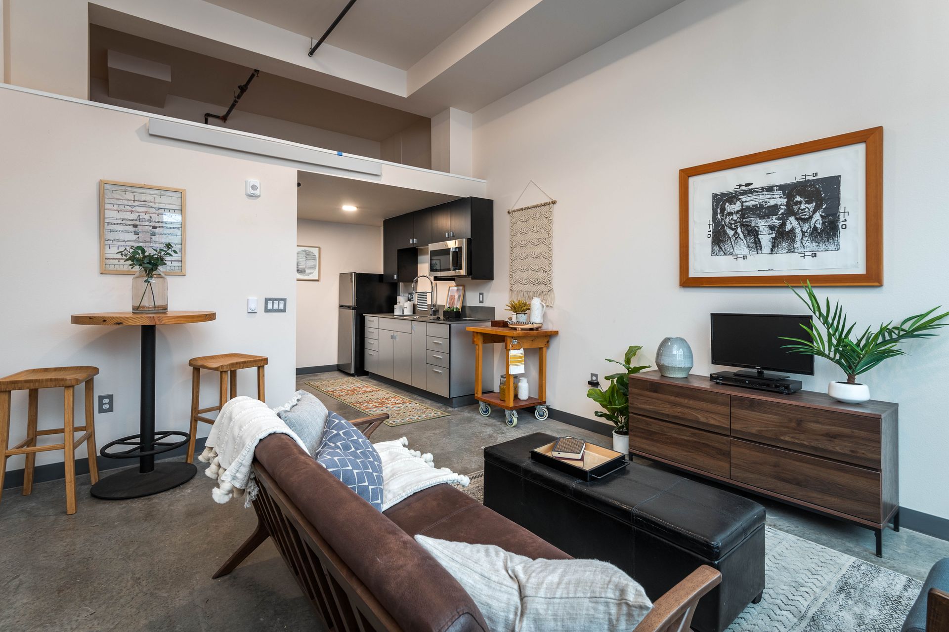 Modern apartment living room with brown leather sofa, open kitchen, and wooden furniture.