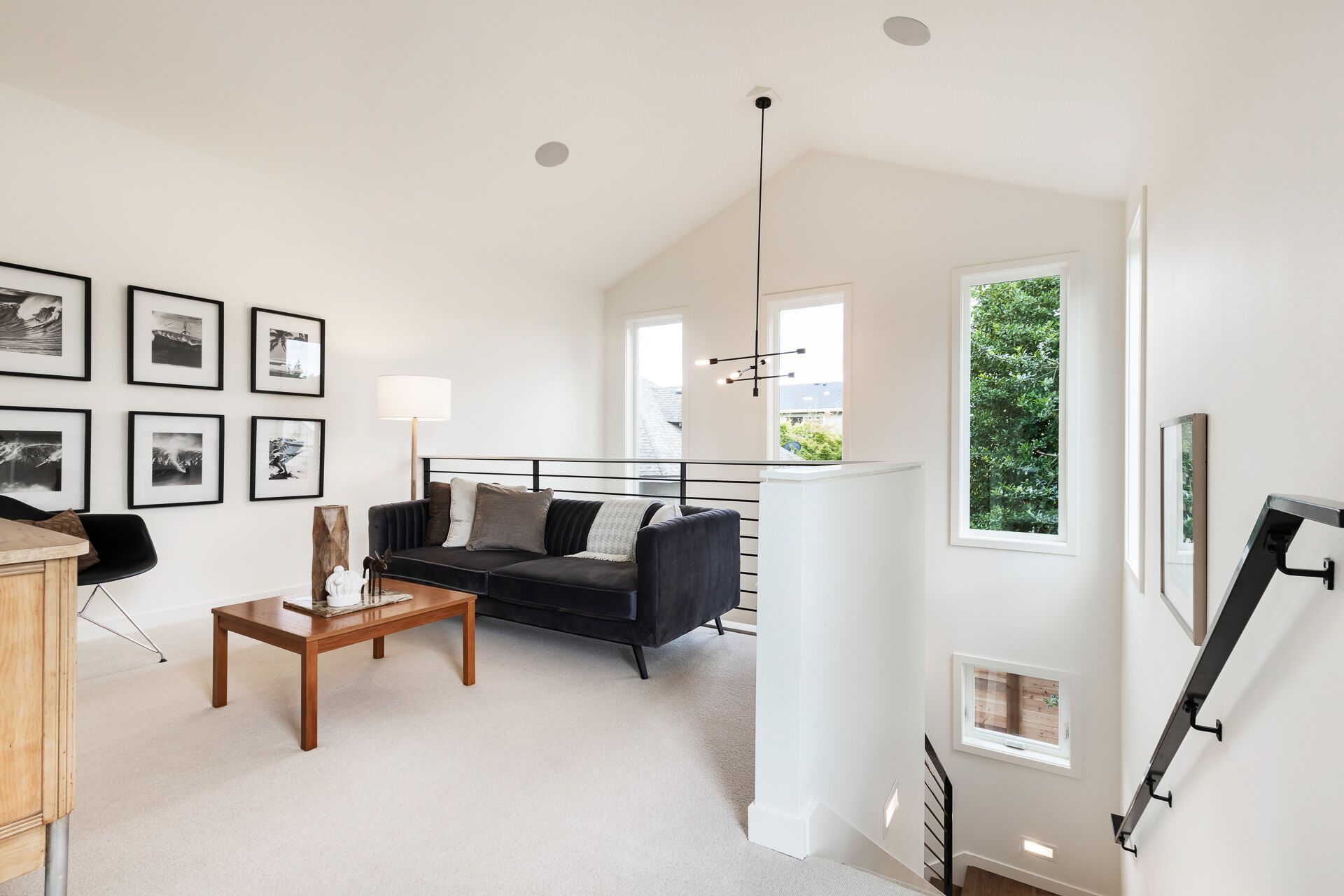 Living room with a black sofa, art, and a staircase. White walls, wood floor, and natural light.