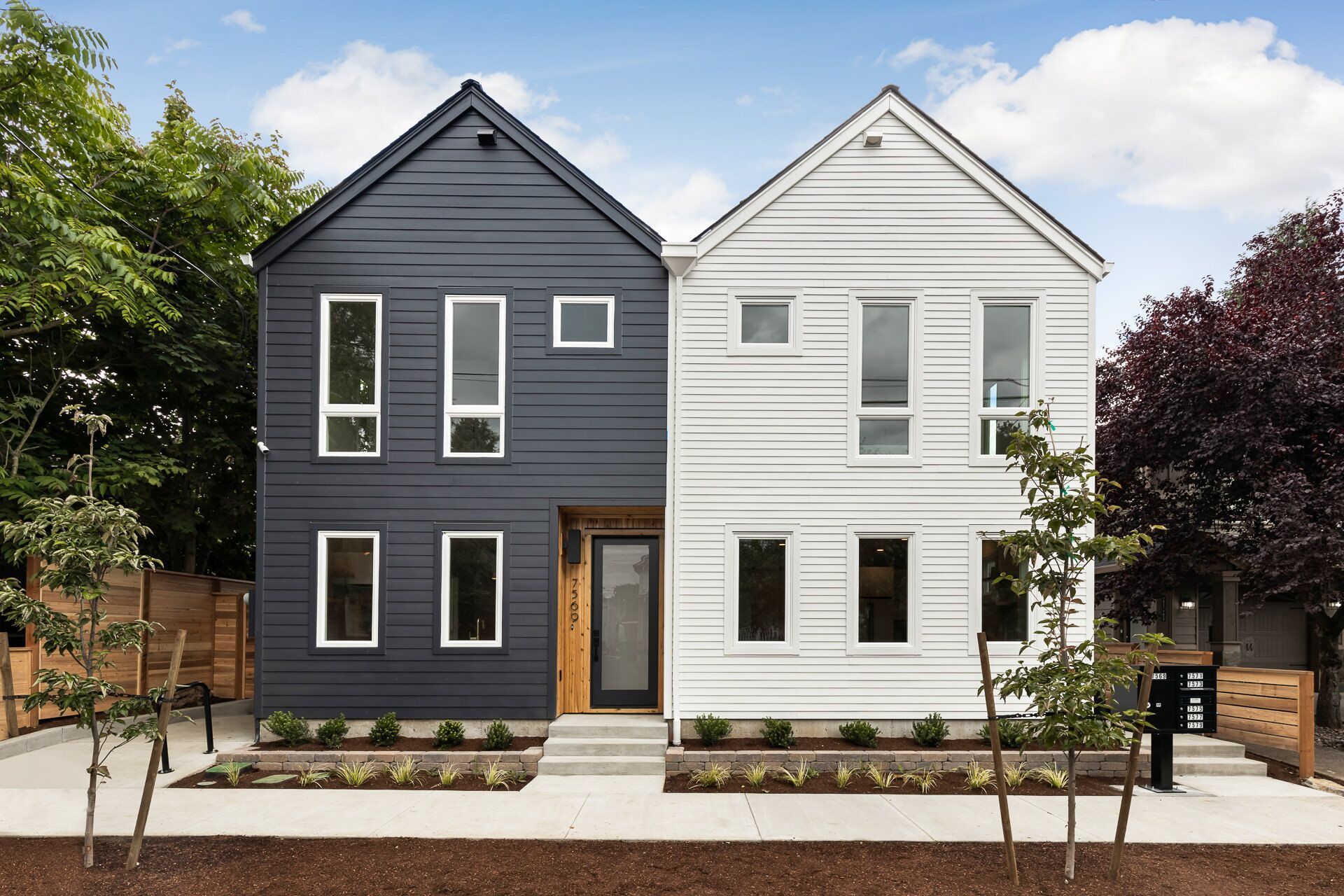 Two modern townhouses, one dark blue, one white, sharing a front door on a sunny day.