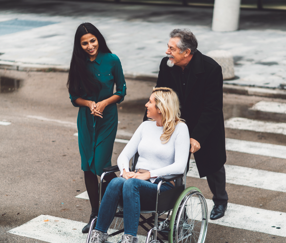 A woman in a wheelchair is being pushed by two people.