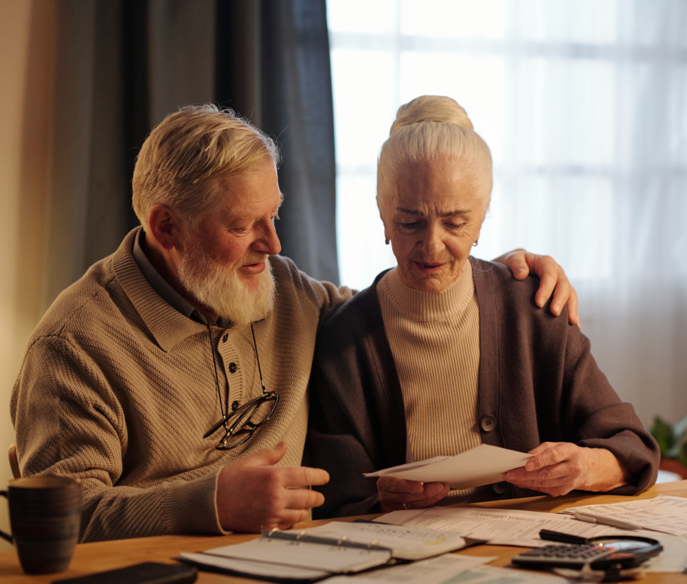 An elderly couple is sitting at a table looking at a piece of paper.