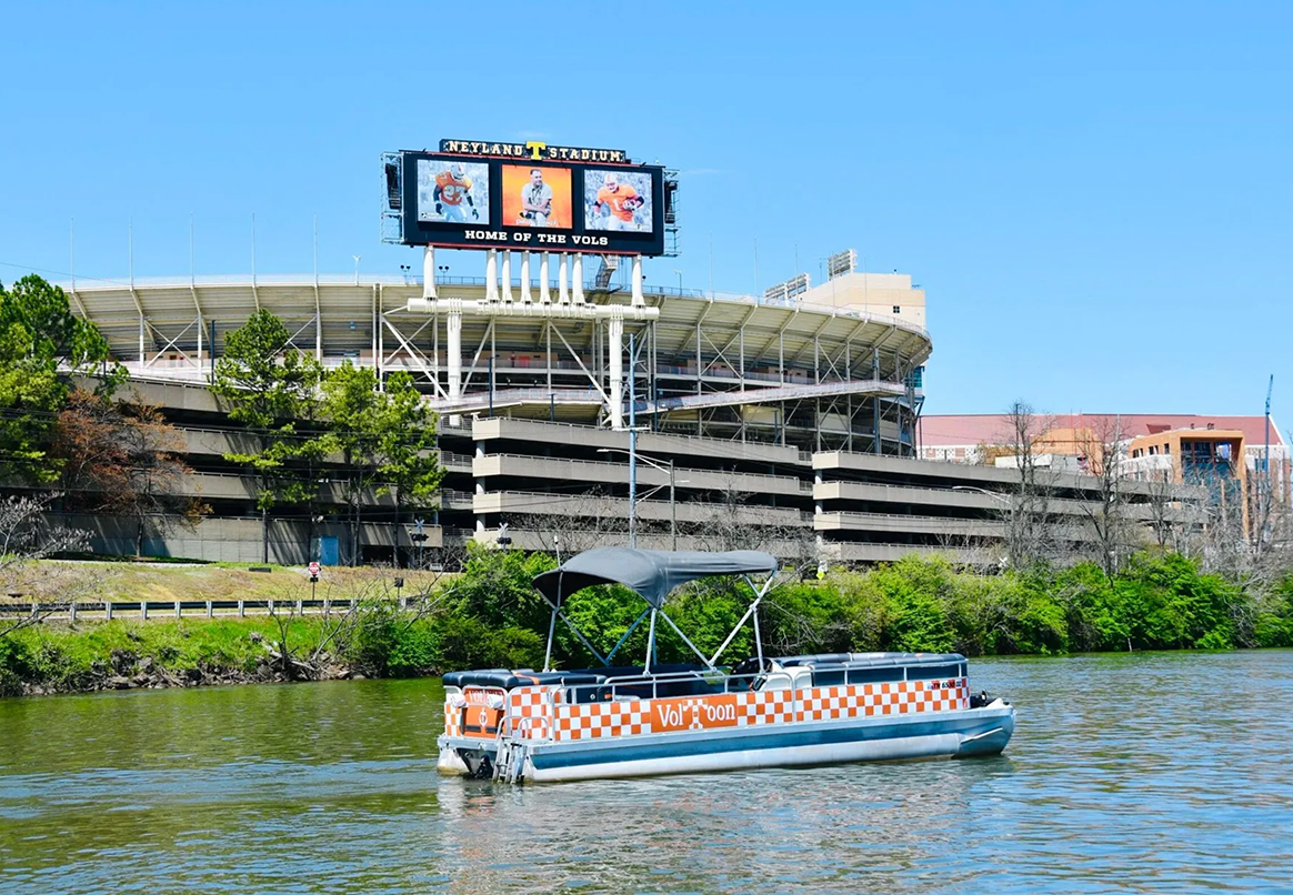 A boat on the water in front of University of Tennessee football stadium with a large scoreboard.