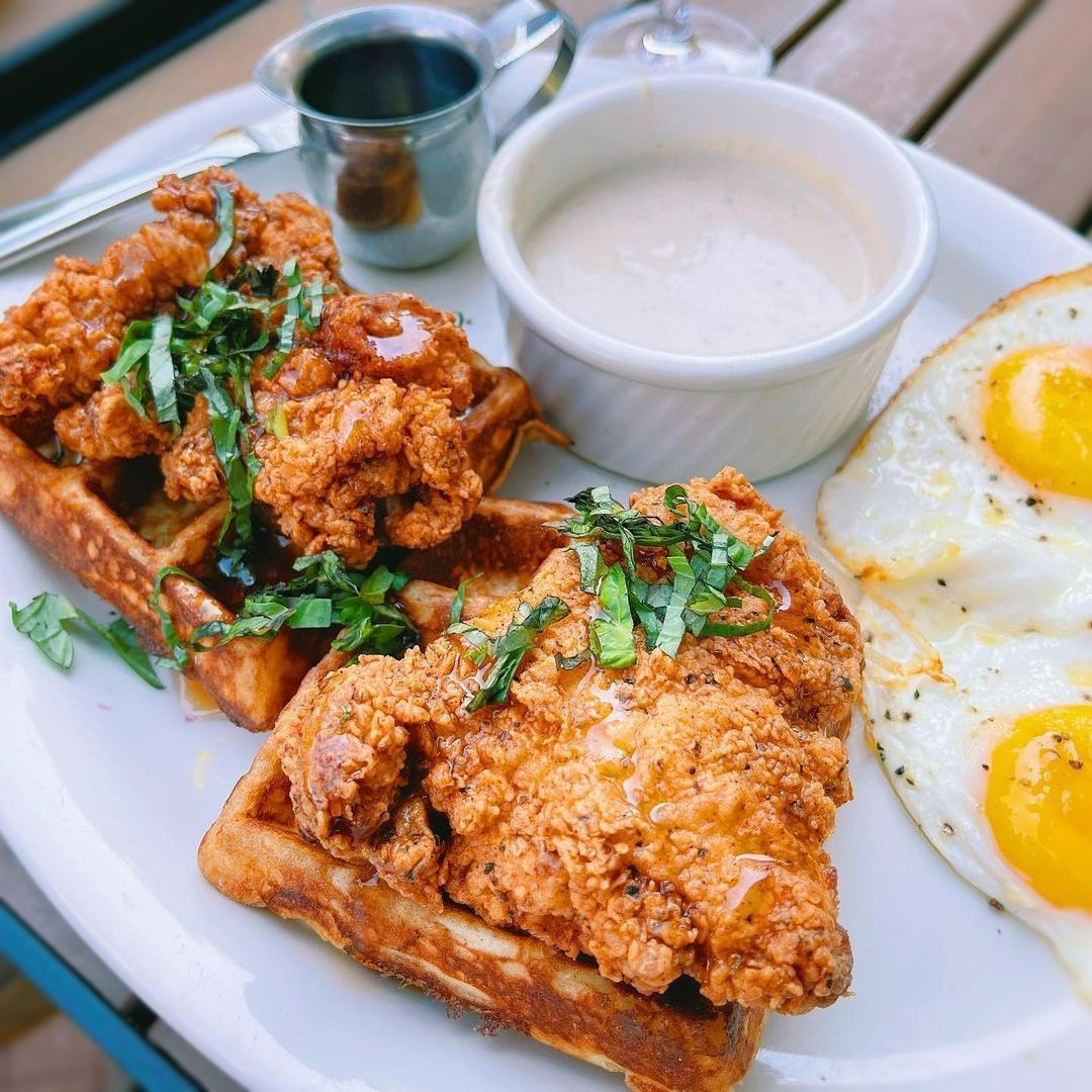Fried chicken and waffles with sunny-side-up eggs and a side of sauce.
