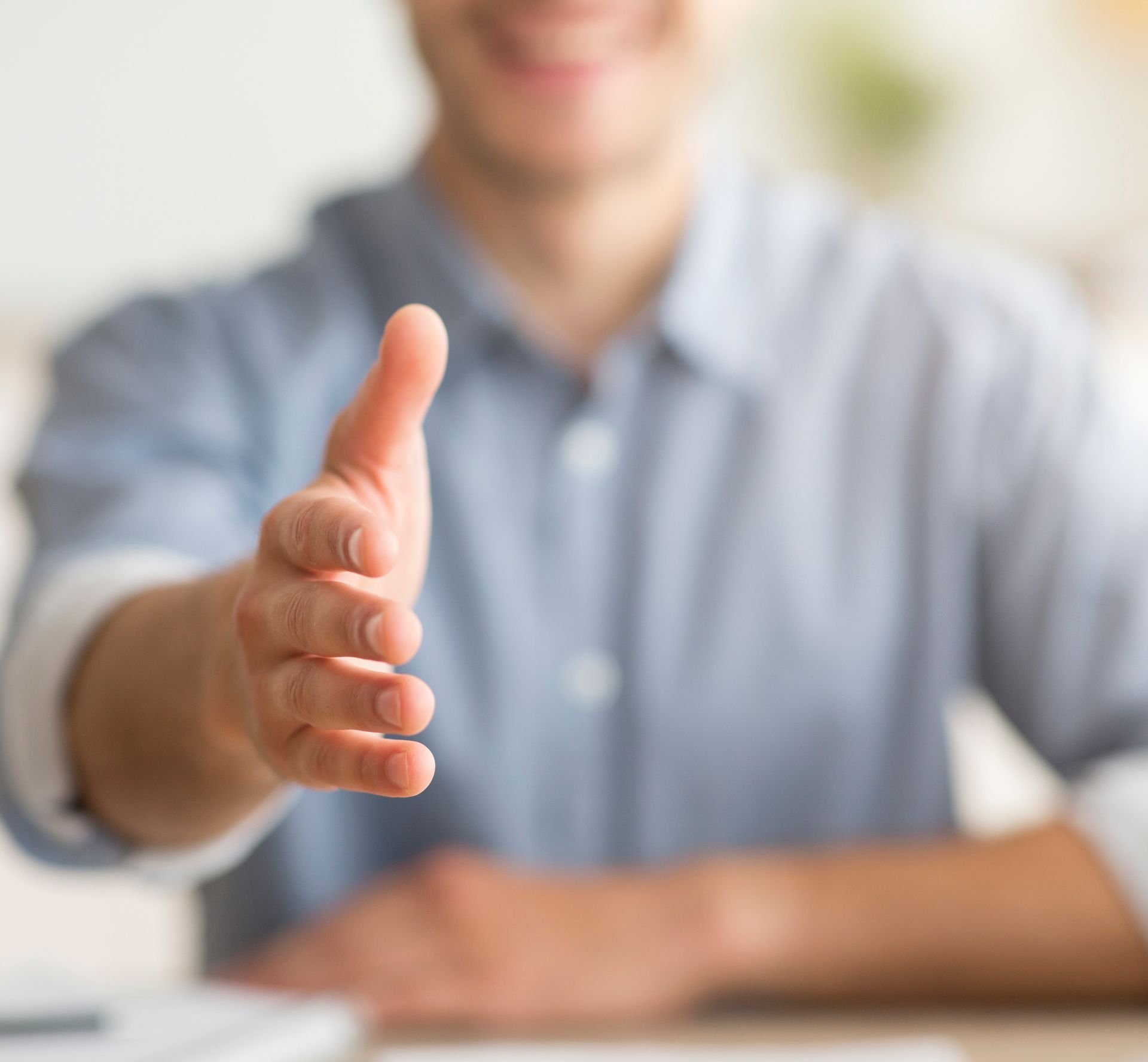 Person in blue shirt extends hand in a handshake gesture.