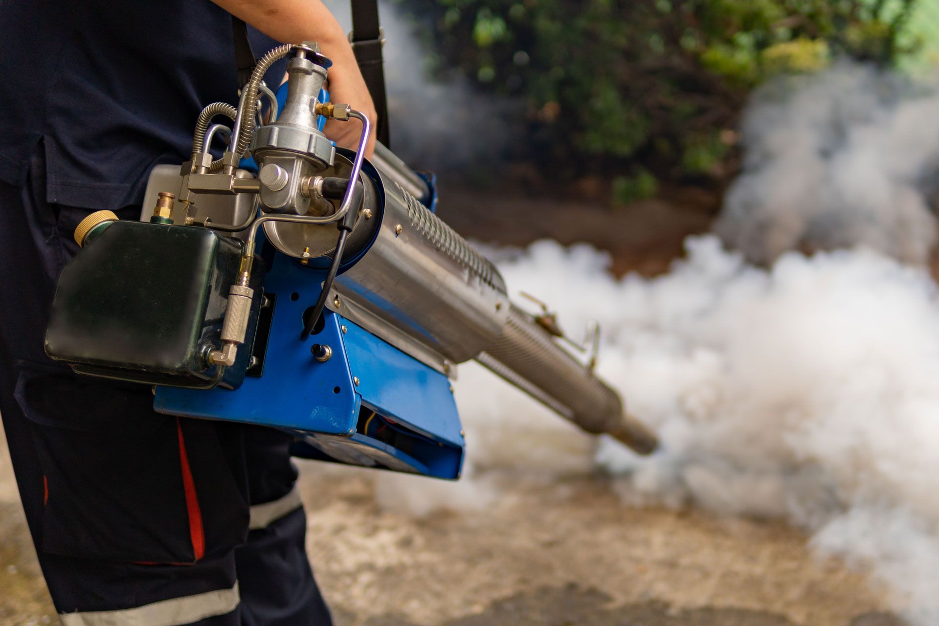 A man is using a machine to spray smoke on the ground.