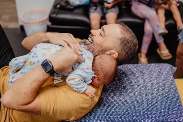 A man is laying on a pillow holding a baby.