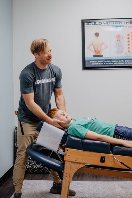 A man is standing next to a boy laying on a table.