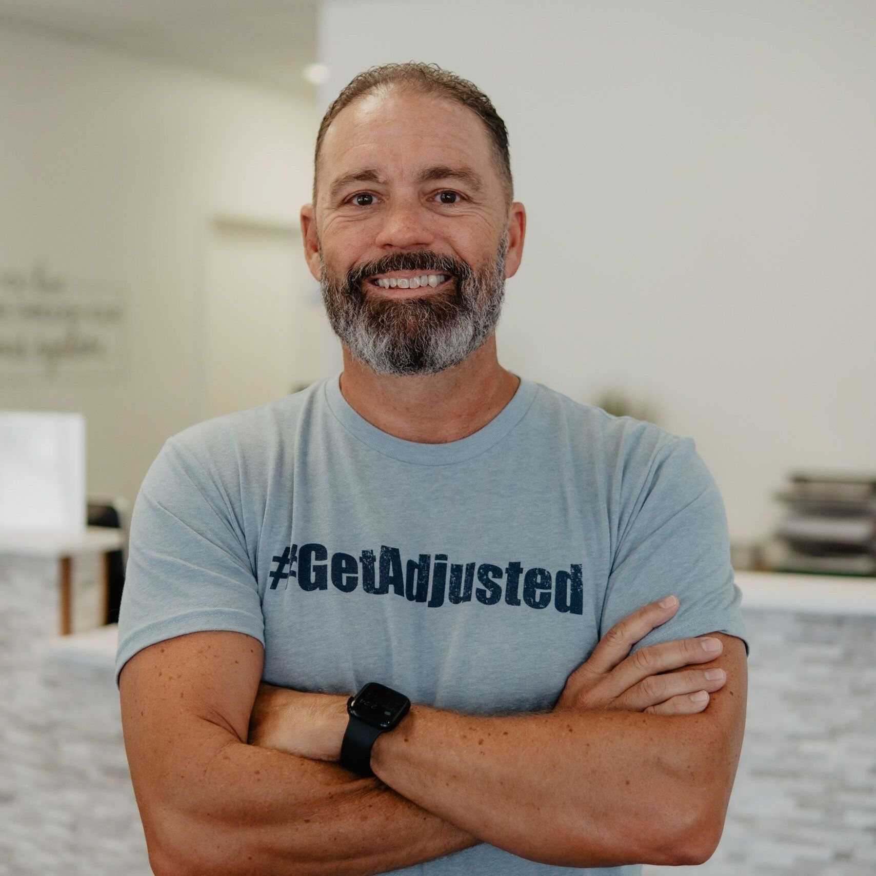 A man with a beard is wearing a shirt that says get adjusted