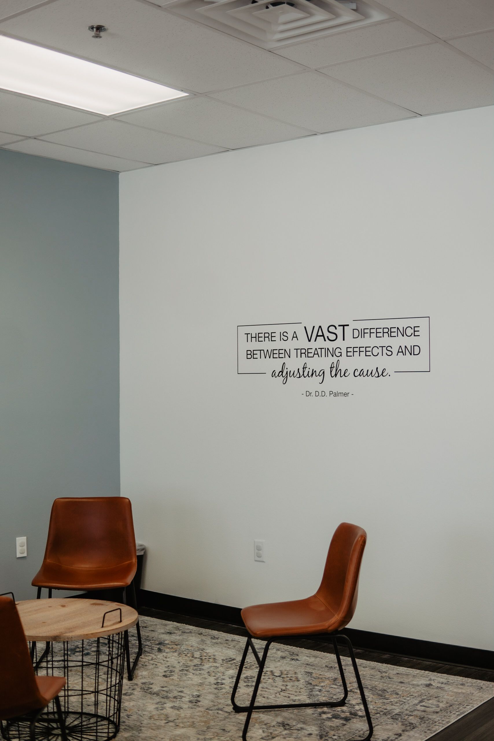 A room with chairs , a table and a wall with a quote on it.