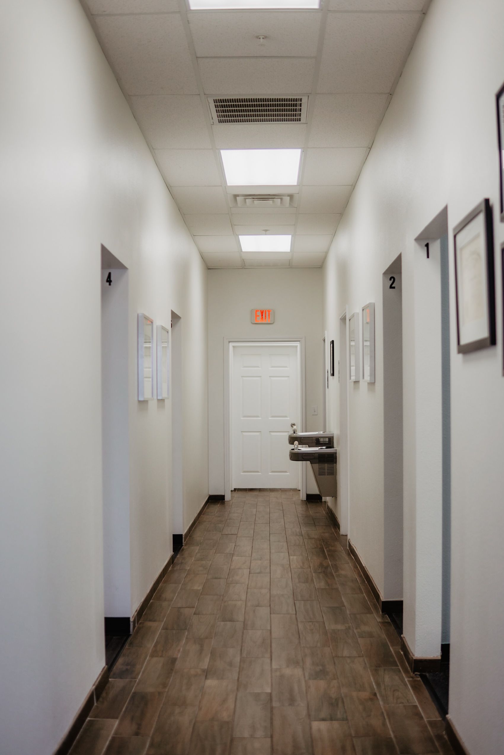 A long hallway with white walls and wooden floors in a hospital.