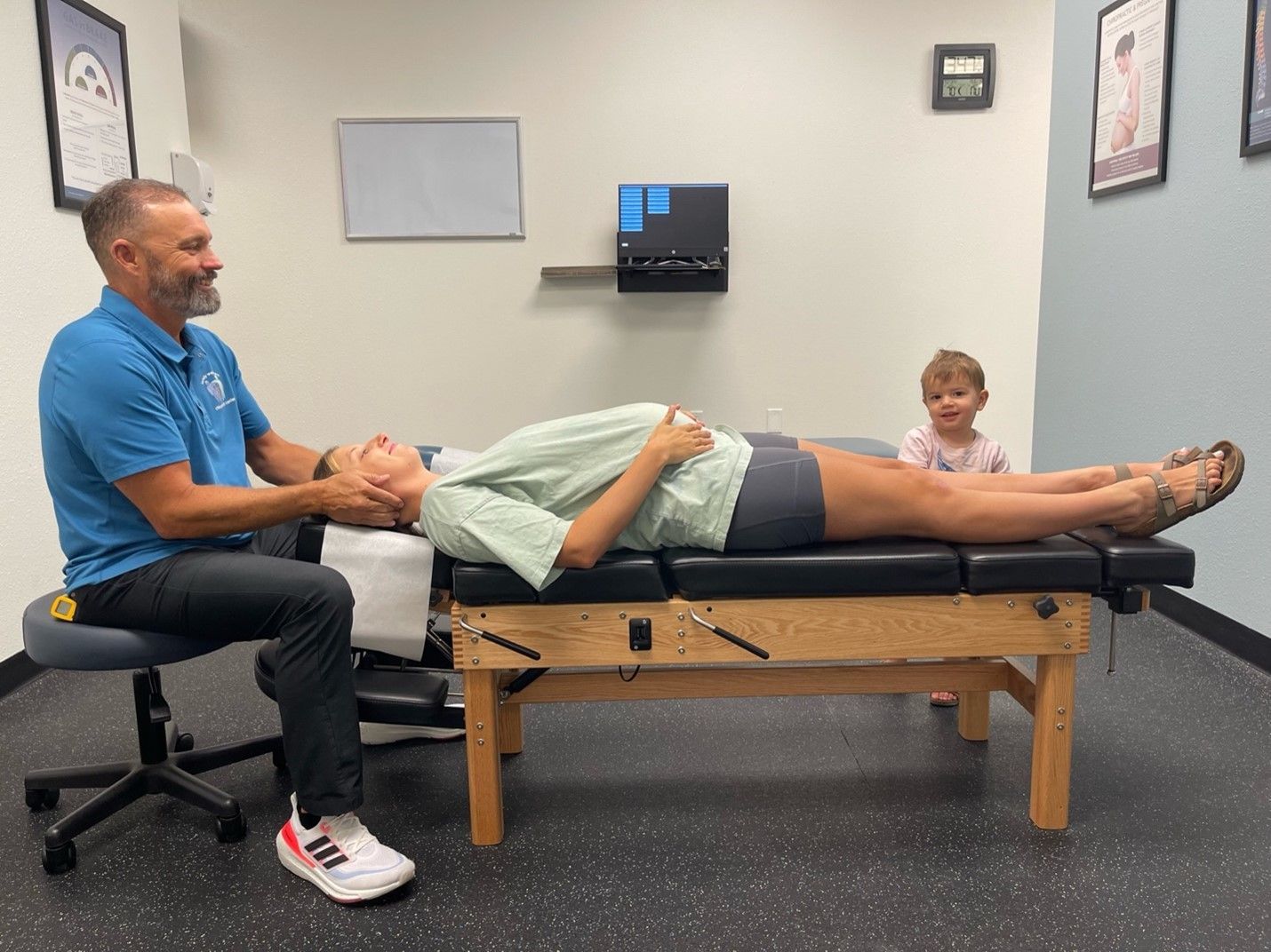A man is sitting on a stool while a child is laying on a table.