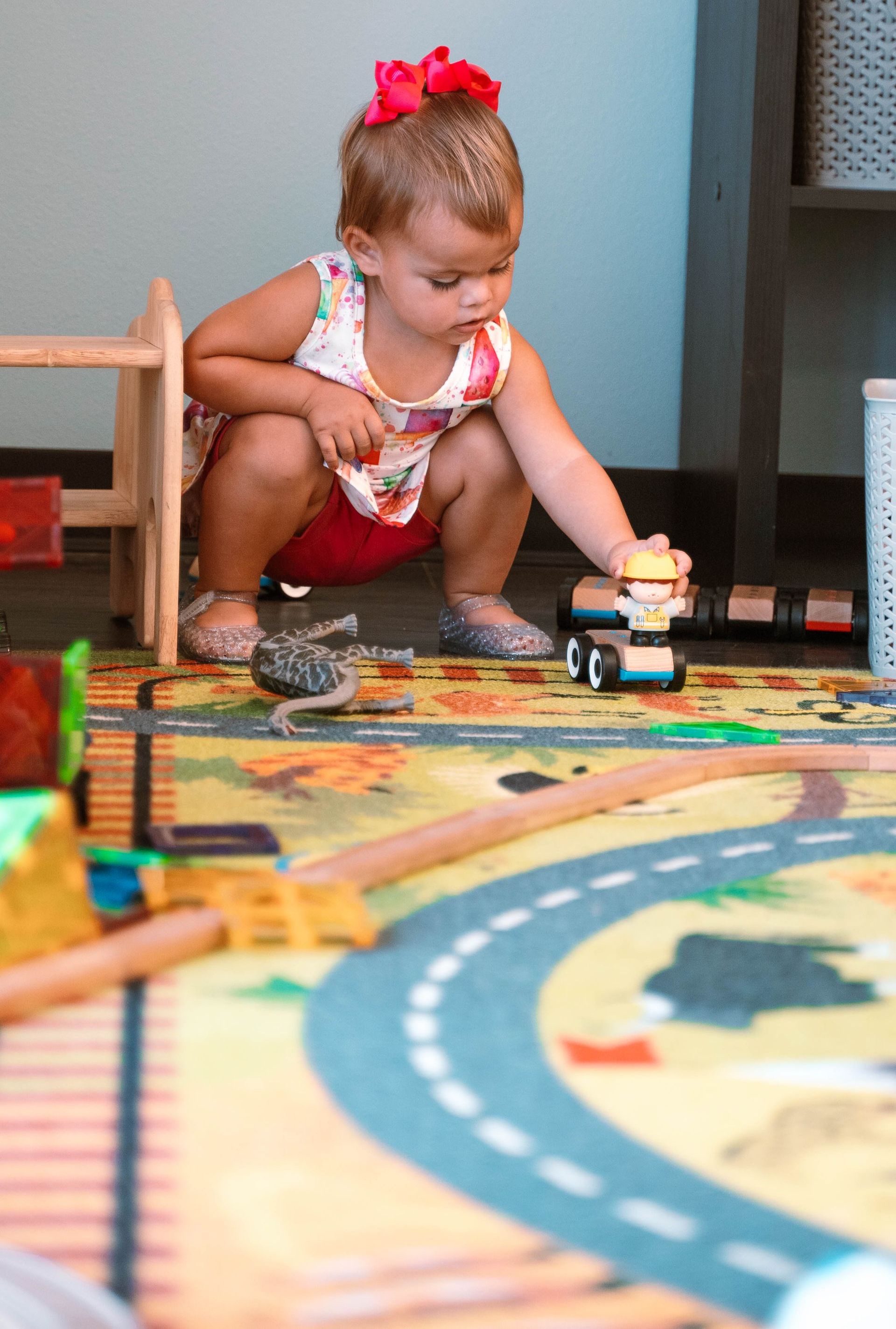 A little girl is kneeling on the floor playing with toys.