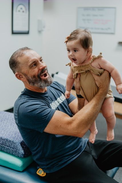A man is holding a baby in his arms while sitting on a table.