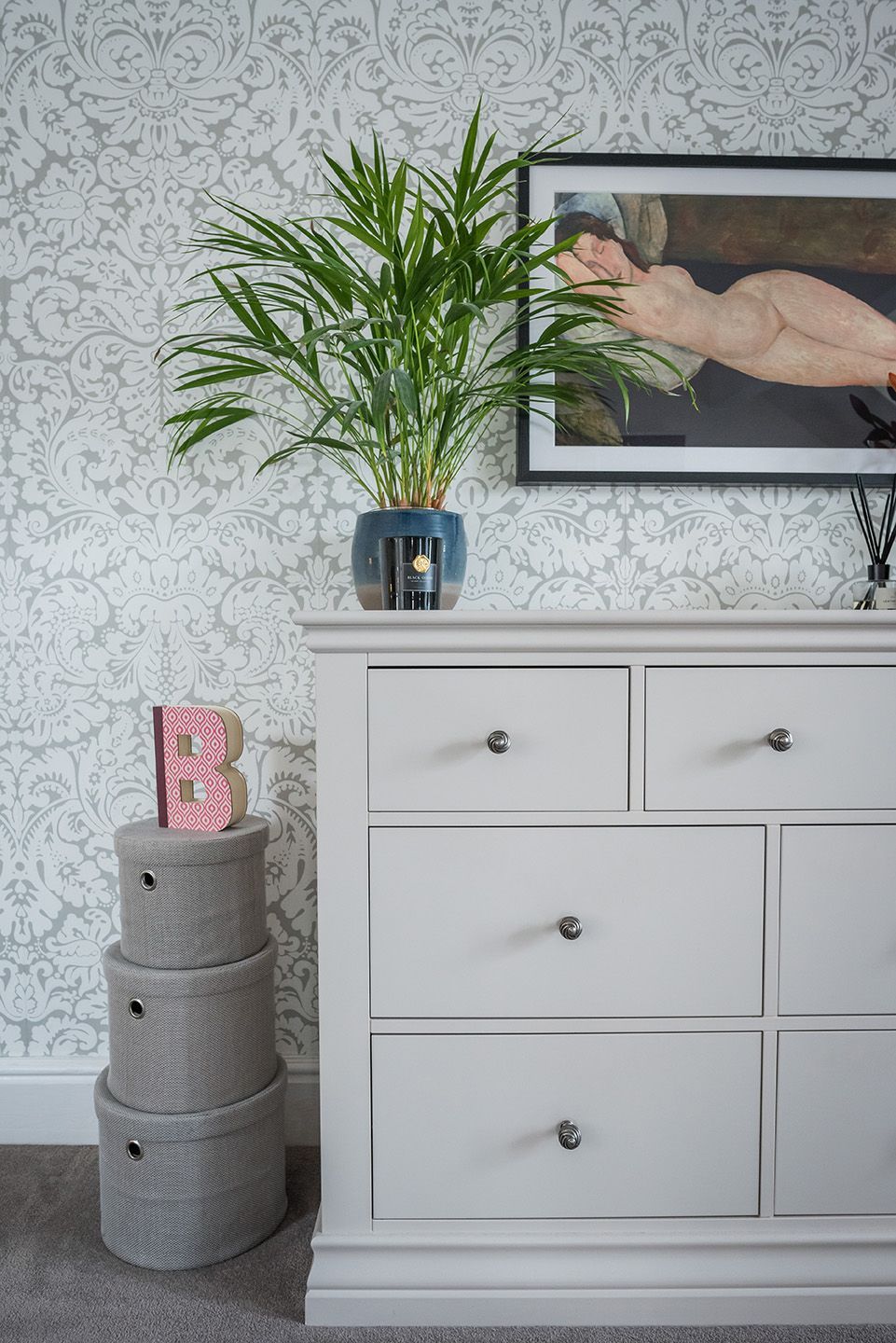 Bedroom grey chest of drawers with stacked boxes, plant and Modigliani nude print