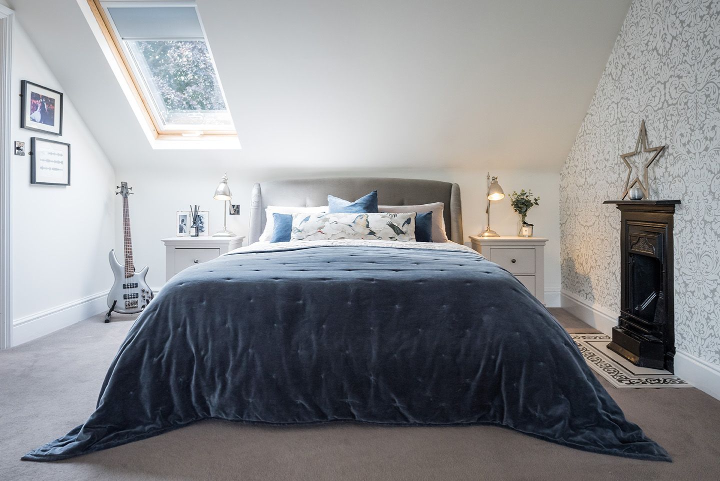 Grey velvet bed with blue velvet throw, cast iron fireplace and electric guitar