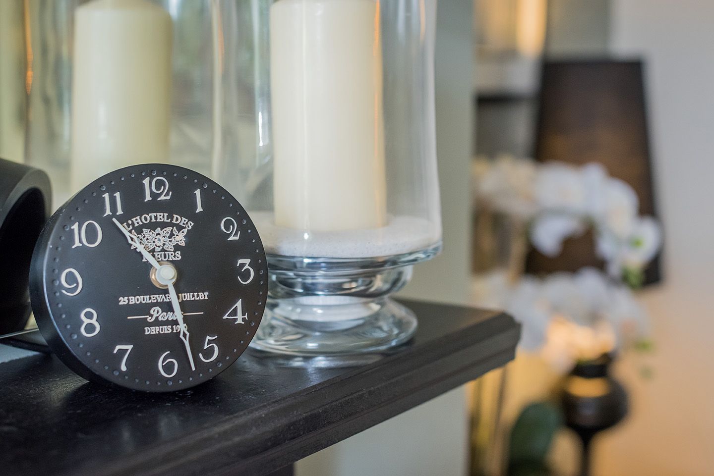 Black clock with glass hurricane lamp on cast iron fireplace