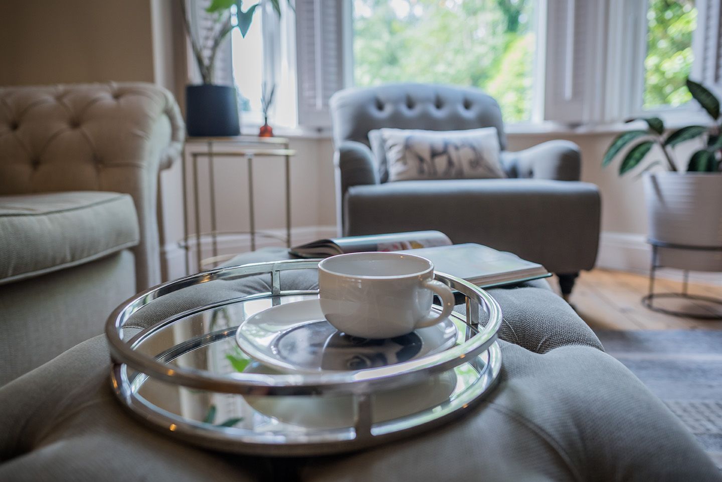 Buttoned grey footstool with chrome tray, book, Fornasetti plate and coffee cup
