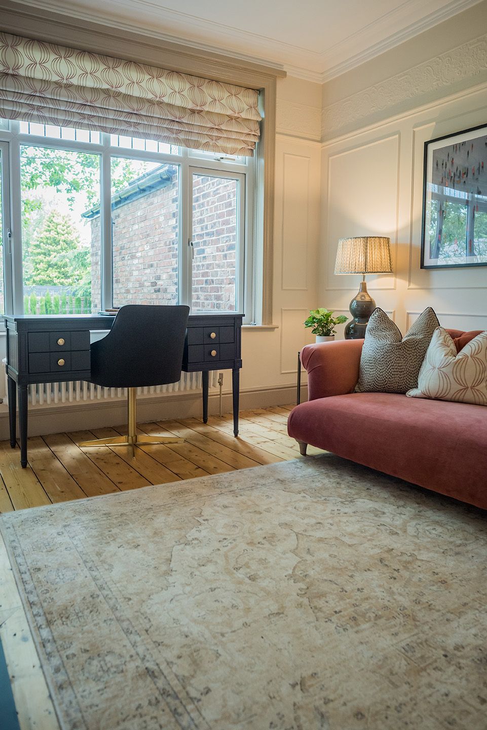Living room pink velvet sofa with taupe cushion and blue wooden desk. Large bespoke roman blind