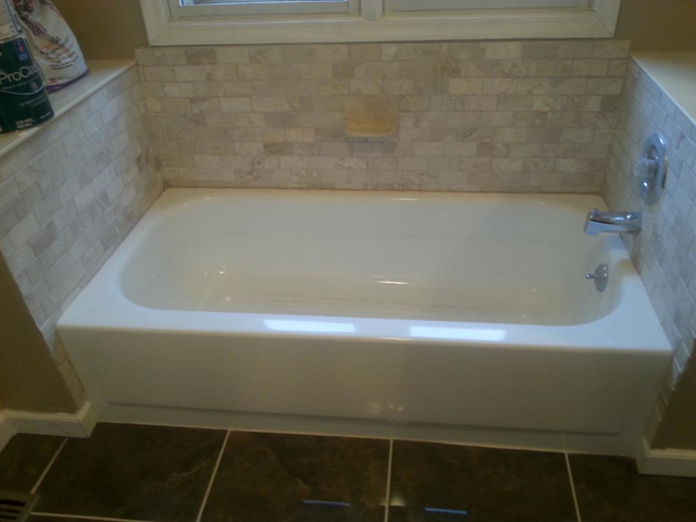 White bathtub with tile surround; dark brown tile floor.