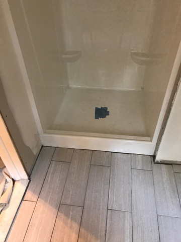 Shower stall with a neutral-colored base, flanked by light gray tiled flooring.