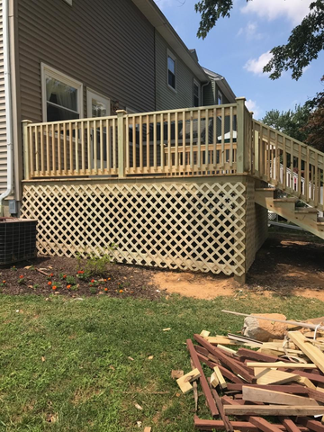 A wooden deck with lattice skirting attached to a house, set in a backyard on a sunny day.