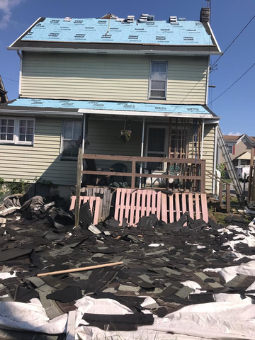 House under construction, roof partially replaced with blue underlayment. Shingles piled in foreground.