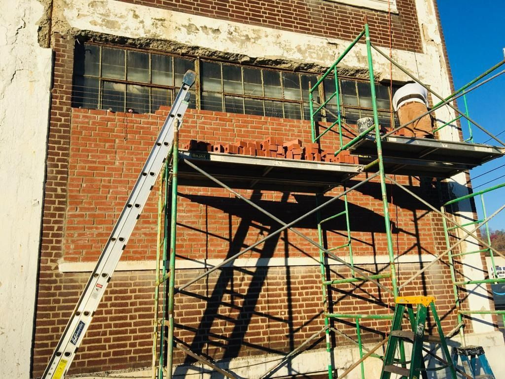 Brick wall repair in progress with scaffolding, ladder, and bricks.