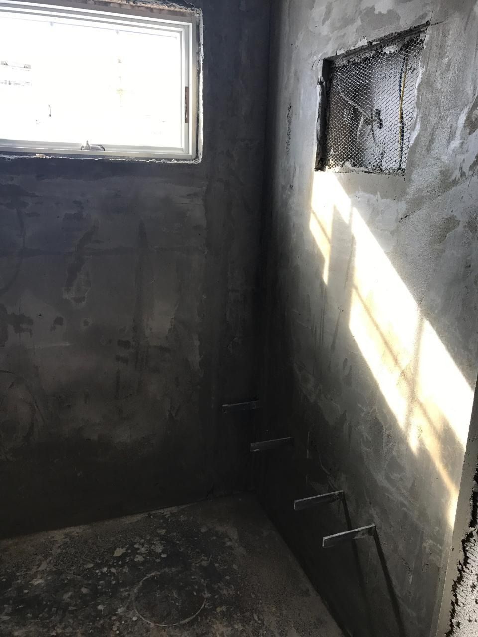 Bathroom under construction, unfinished concrete walls, window, and plumbing fixtures.