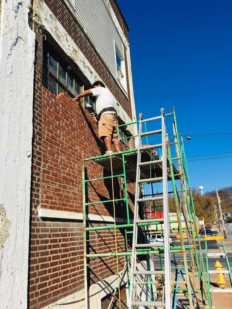 Man on scaffolding repairs brick wall of building under a blue sky.
