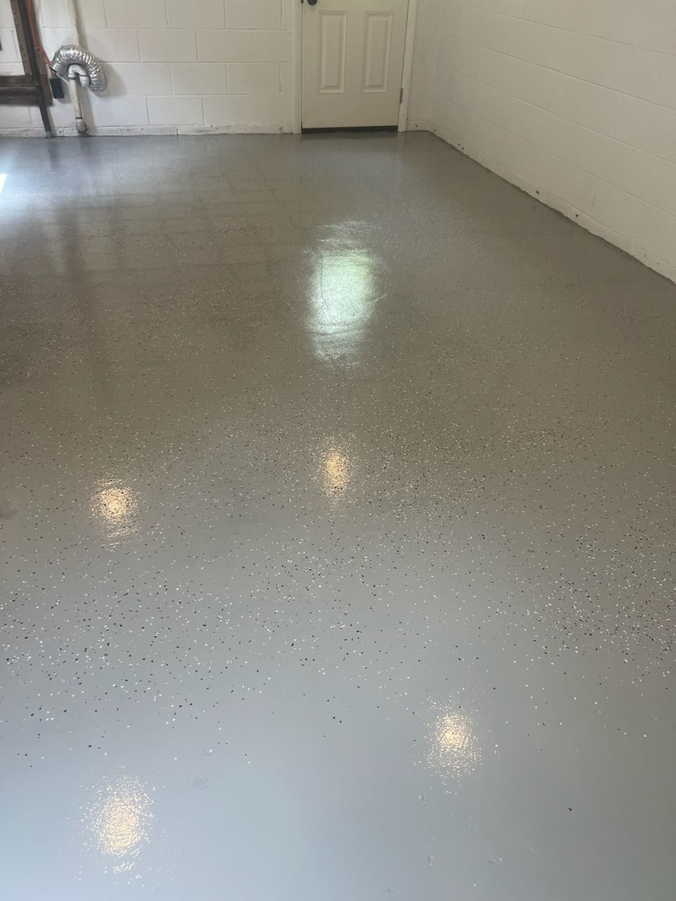 Gray epoxy-coated garage floor with speckled chips, reflecting light. White walls and a door are visible.