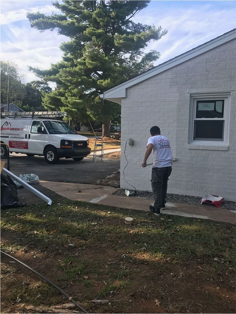 A worker outside a white brick building walks towards it, truck and tree visible.