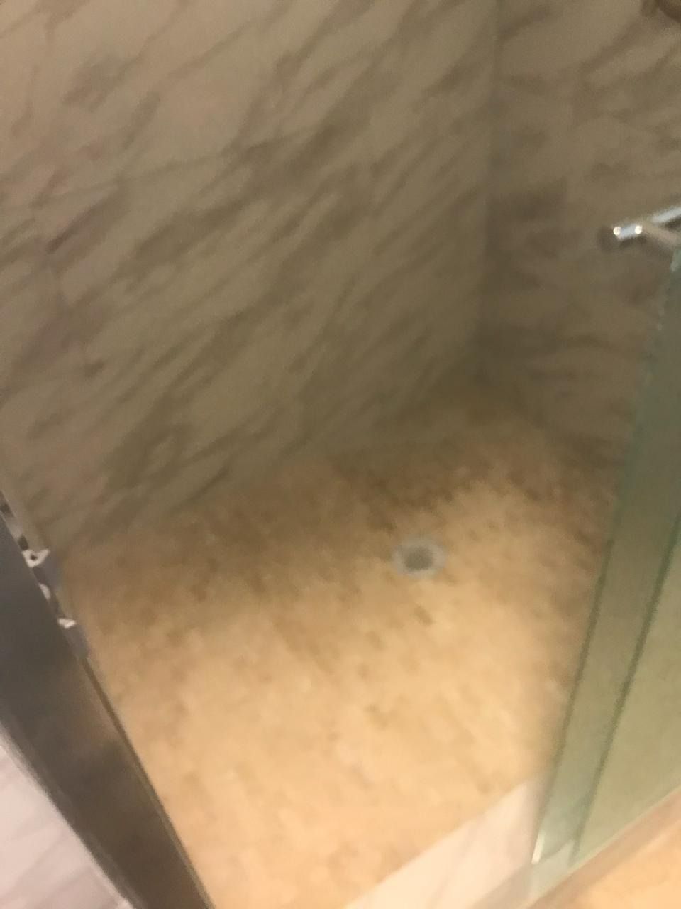 Shower with beige and white marble walls and floor, glass door, and chrome fixtures.