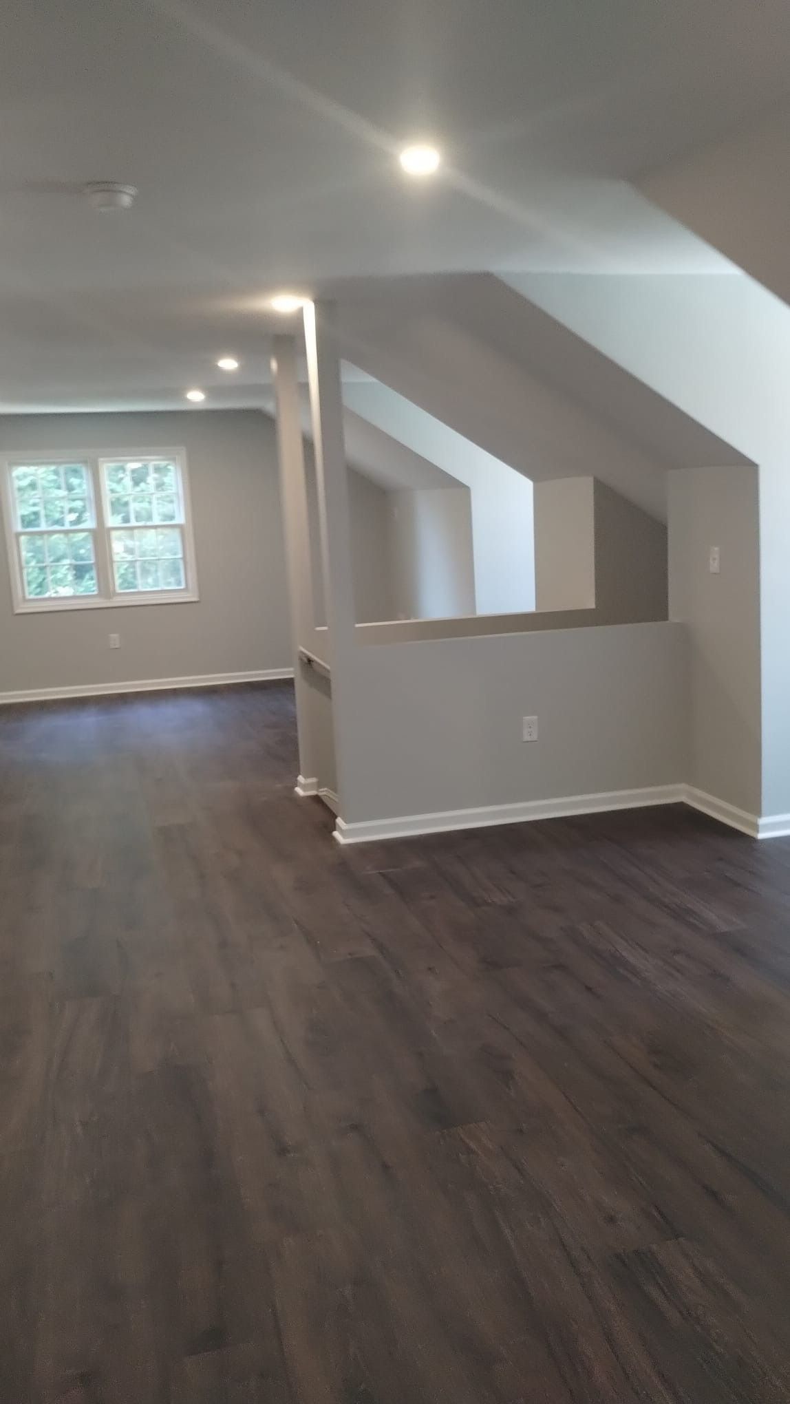 Interior view of a room with dark wood floors, grey walls, and a partial wall with a window in the background.