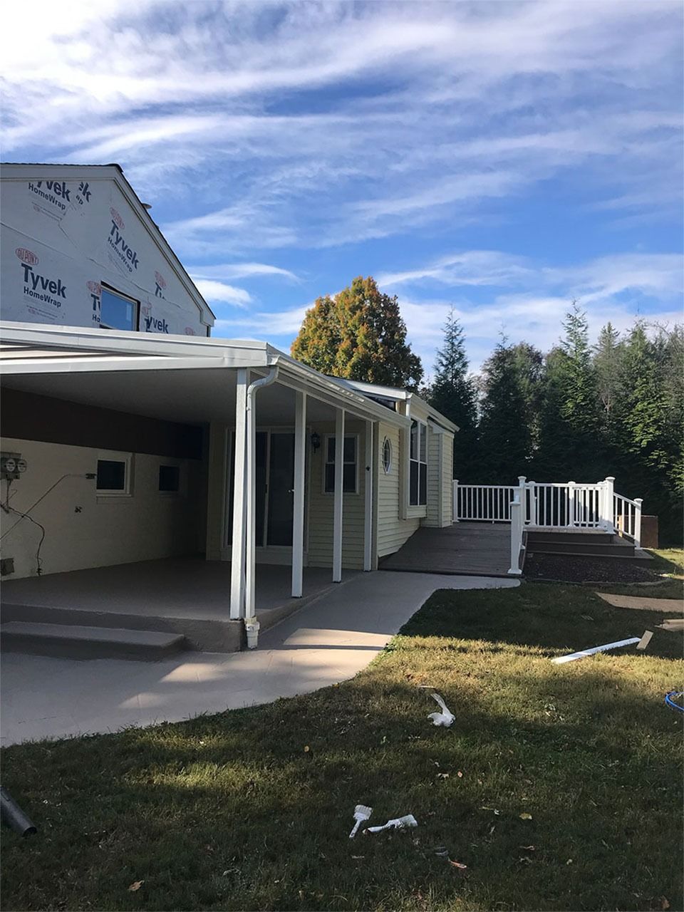 Exterior view of a light yellow house with a covered patio and a wooden deck on a sunny day.