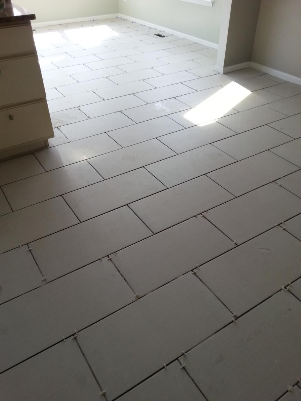 Tiled floor with light gray rectangular tiles laid in a brick pattern in a room with a cabinet.