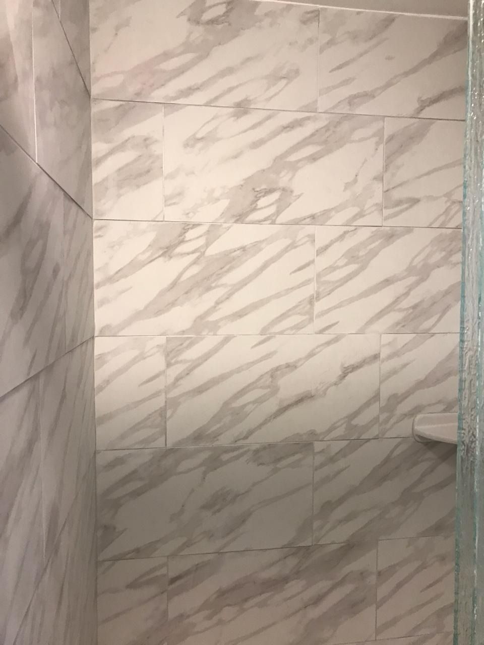 White marble tiled shower with glass door and built-in shelf.