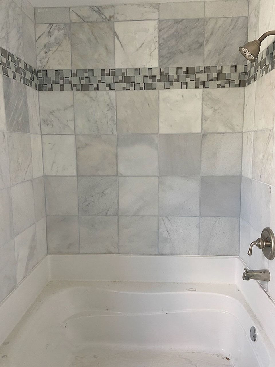 White-tiled shower with a mosaic border above a white bathtub. Brushed nickel fixtures.