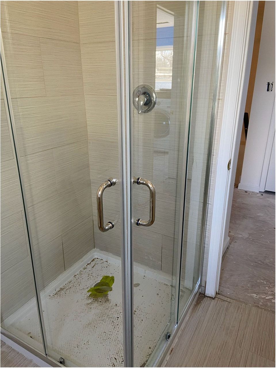 Corner shower with glass doors, stainless steel handles, and cream-colored tiles.