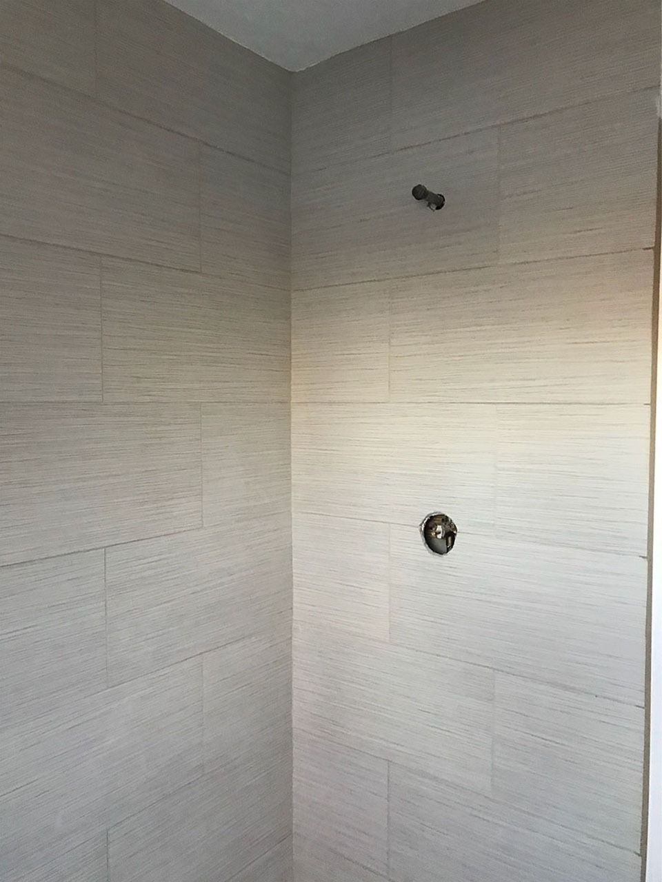 Beige tiled shower with a showerhead and faucet.