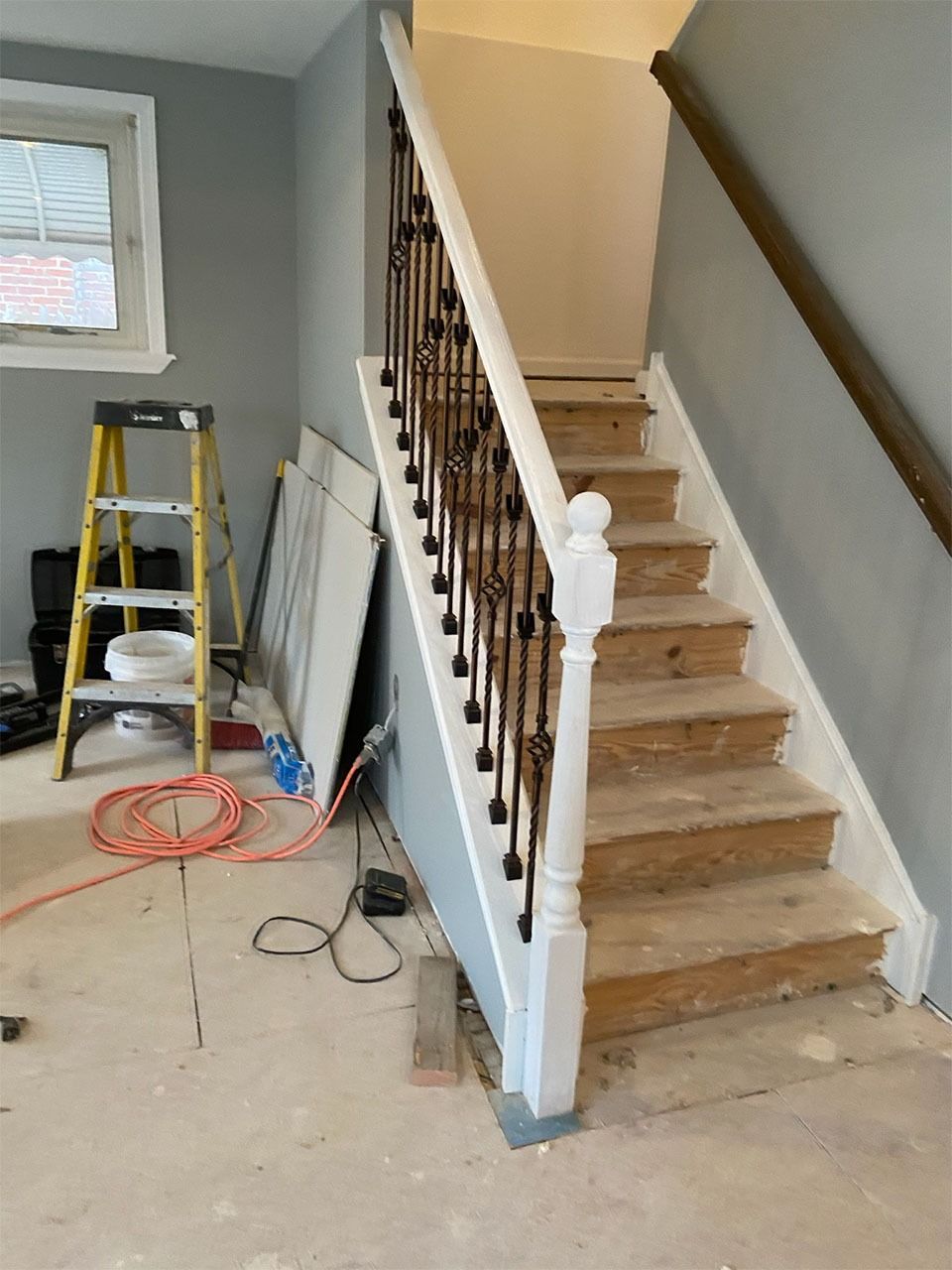 Staircase with white balusters and dark iron spindles under construction, tools and ladder nearby.
