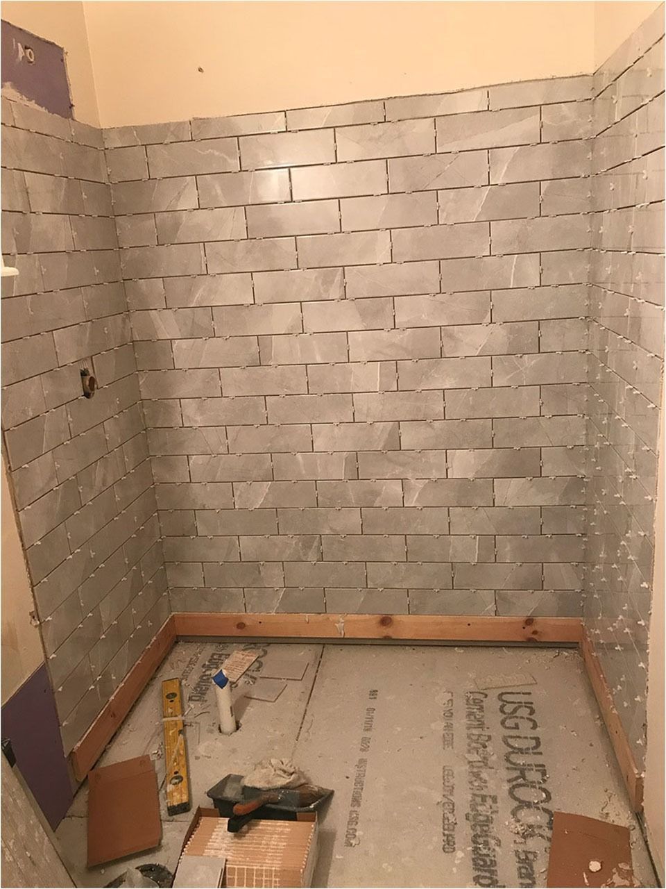 Shower under construction: gray tile, wooden base, tools on the floor.