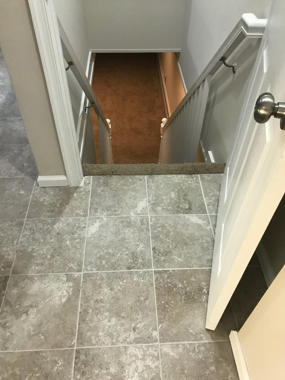 Tile floor leads to a carpeted staircase going down, with a door partially open on the right.