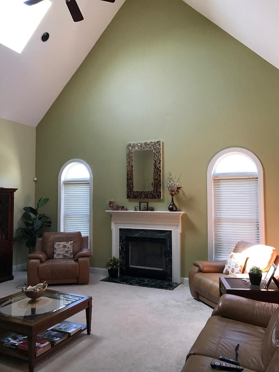 Living room with vaulted ceiling, fireplace, two arched windows, and brown leather furniture.
