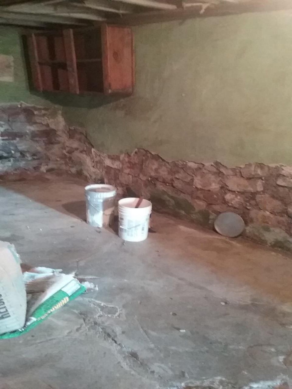 Basement with stone wall, concrete floor, buckets, and wall-mounted cabinet.