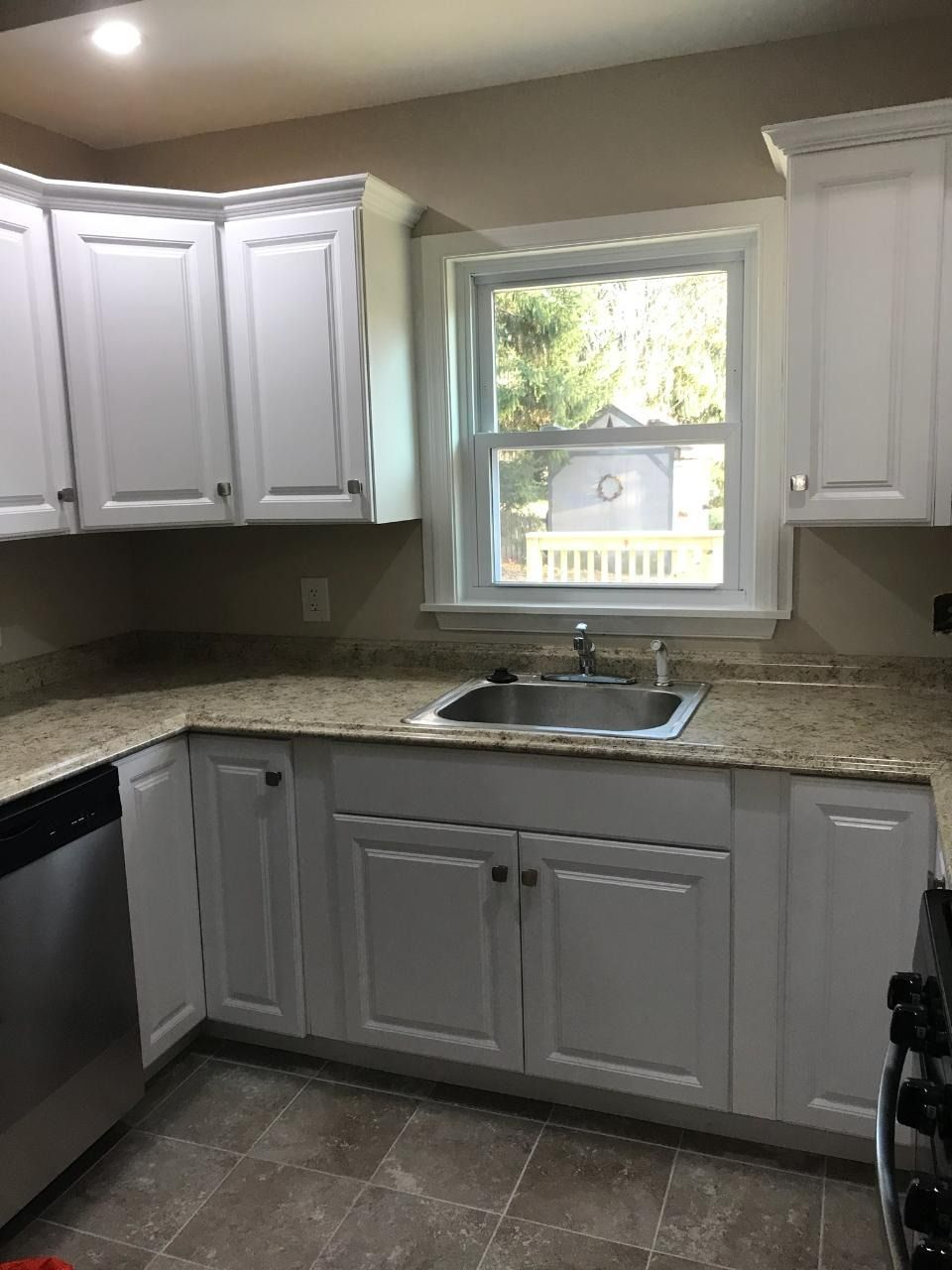 White kitchen cabinets with light granite countertops, stainless steel sink, and a window.